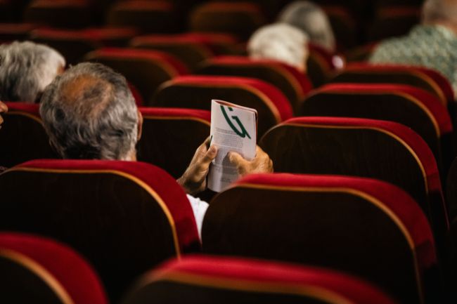 un homme assis dans un fauteuil de cinéma tient une brochure 