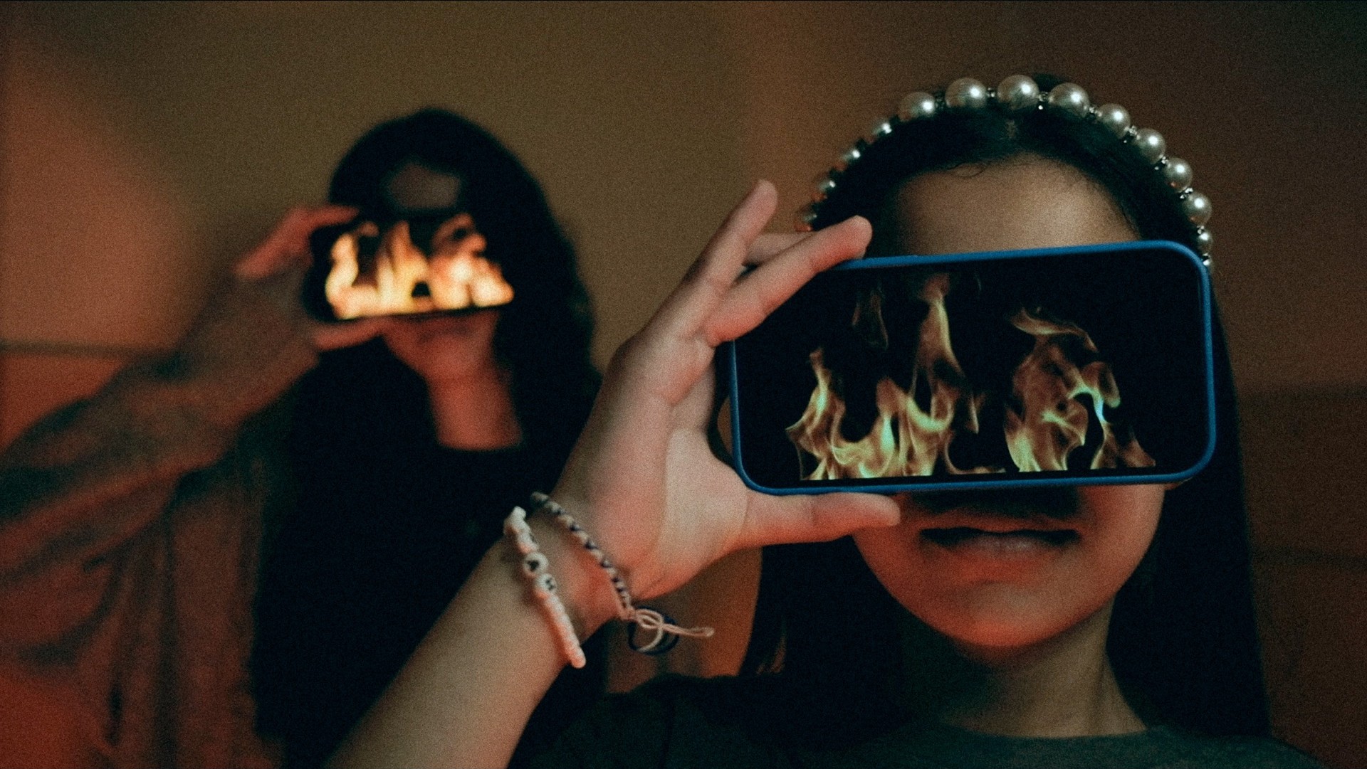 Photo de deux jeunes femmes qui tiennent un smartphobne devant les yeux sur lesquels sont diffusés des flames