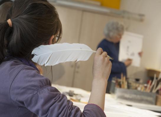 Une petit fille de dos écrit avec une plume 