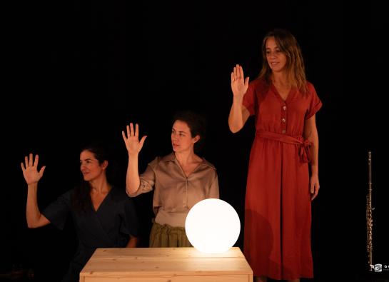 trois femmes lèvent la main. Une boule lumineuse est posée sur une table