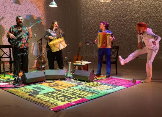 des musiciens jouent sur des tapis colorés. A droite, un homme vêtu de blanc tel un trappeur
