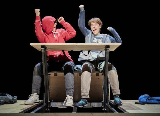Deux jeunes garçons font des gestes de victoire attablés à un bureau