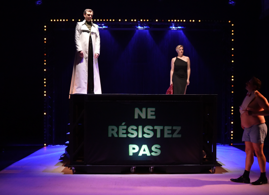 Deux personnes debout sur praticable sur lequel est affichée ne résiste pas. Une troisième personne au sol, regarde ce message.