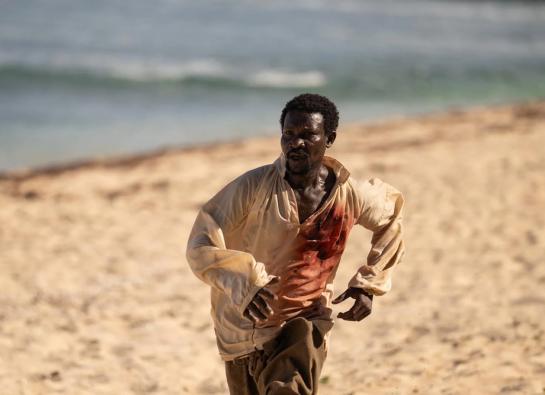 un homme noir court sur la plage avec une chemise ensanglantée