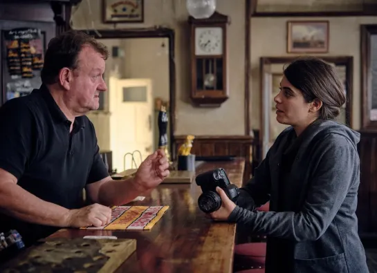 une femme avec un appareil photo parle à un homme dans un bar