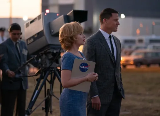 une femme tient un dossier NASA à côté d'un homme avec une caméra en arrière plan